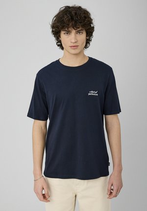 T-shirt en coton bleu marine à manches courtes, col rond, avec une broderie en texte blanc "une dose de perfection" sur la partie gauche de la poitrine.