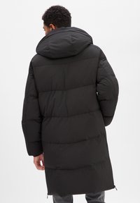 Schwarzer Steppmantel mit großer Kapuze, Steppmuster, langen Ärmeln und seitlichen Reißverschlüssen, gefertigt aus glattem, wasserabweisendem Stoff.