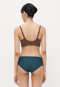 Sutiã castanho com alças ajustáveis e fecho de gancho, combinado com peças íntimas de cintura alta em teal escuro, apresentando um tecido suave e um design simples.