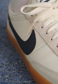 Αθλητικά παπούτσια Nike με κρεμ δερμάτινη επιφάνεια, ναυτικό λογότυπο, μπεζ κορδόνια και διαφανή σόλα από καουτσούκ. Κοντινή λήψη του αριστερού παπουτσιού.