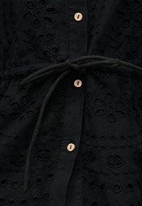 Black fabric with embroidered floral patterns, light brown buttons, and a tied narrow fabric belt at the waist.