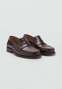 Mocasini din piele maro cu o finisare netedă, vârf rotund și cusături decorative pe partea din față. Talpă din cauciuc pentru durabilitate.