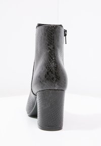 Botines de tacón alto negros con un patrón texturizado de piel de serpiente, cierre lateral con cremallera y un robusto tacón cuadrado. Acabado liso y forma redondeada.