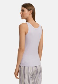 Fialový top na ramínka s žebrovanou texturou, širokými ramínky a kulatým výstřihem. V kombinaci s pruhovanými pyžamovými kalhotami v krémové barvě a světle fialové.