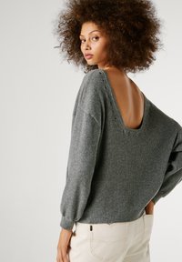 Pelēks ribots džemperis ar dziļu V formas aizmuguri, apaļu kakla izgriezumu un puffētiem piedurkņu galiem. Ievērojami acu caurumi pa aizmugures kakla izgriezumu.