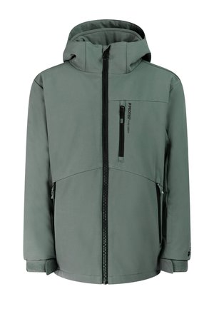 Jongen die een groene winterjas met capuchon, zwarte broek en zwarte laarzen draagt, staat voor een effen lichte achtergrond.
