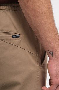 Shorts marron clair avec une taille élastique, dotés d'une poche sur le côté et d'une petite étiquette noire de marque Volcom cousue sur le côté gauche.