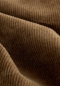 Tessuto ribbed marrone che mostra una superficie testurizzata con linee sottili che corrono in parallelo. Il materiale appare morbido e peloso, creando un aspetto caldo e accogliente.