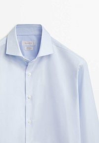 Lichtblauwe langemouwen shirt gemaakt van gladde stof. Heeft een puntige kraag en een knoopsluiting met contrasterende witte knopen.