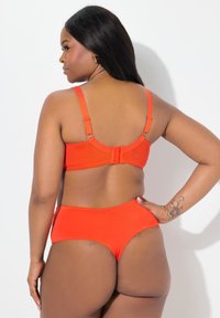Rode bikini-set met een bralette-top met verstelbare bandjes en een haaksluiting, gecombineerd met high-waisted bottom, zachte textuur.