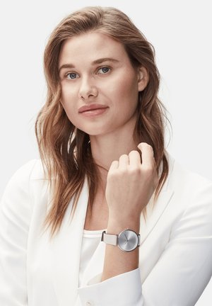 Silberner Edelstahluhren mit rundem Ziffernblatt und minimalistischem Design; verfügt über ein hellgraues strukturiertes Armband.
