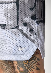 Nike træningsskjorte lavet af åndbart mesh, med et fremtrædende gråt og hvidt abstrakt mønster samt et sølvfarvet logo nederst.