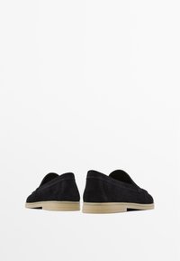 Scarpe slip-on nere in suede con un design minimalista, caratterizzate da una suola in gomma tan chiaro e cuciture sottili lungo i bordi.