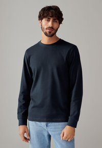 T-shirt a maniche lunghe blu navy in cotone morbido, con collo a giro e polsini a coste, indossato con jeans di denim blu chiaro.