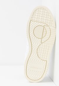 Vit sneakersula med texturerade mönster, med en rund sektion och präglad Adidas-logotyp. Materialet verkar gummiliknande med en slät yta.