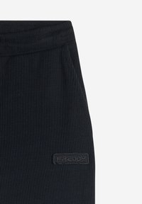 Pantaloni della tuta neri a costine con una cintura elastica, dotati di tasche laterali e un tessuto texturizzato. È visibile un'etichetta con il logo "FREDDY" nera.