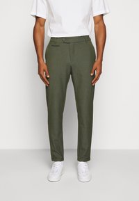 Olivgröna chinos i textil med strukturerad yta, med slim fit, knappstängning och sidofickor, ihop med vita sneakers.