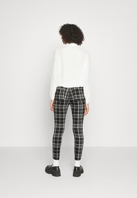 Leggings ajustados em padrão xadrez preto e branco com uma cintura alta, combinados com uma t-shirt de manga longa branca. O calçado é de sapatos pretos robustos.