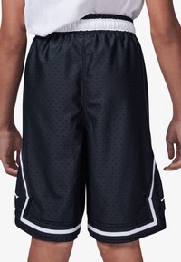 Zwarte basketbalkorte gemaakt van geperforeerde stof, met een witte elastische tailleband en witte zijdelen met een klein logo.