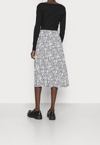 Top lungo a maniche lunghe nero a coste abbinato a una gonna midi bianca con stampa floreale. Le calzature sono un paio di scarpe platform nere chunky.