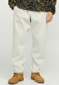 Lysegrå sweatpants med en afslappet pasform, der har en glat tekstur og elastiske manchetter, parret med brune snørebåndsstøvler.