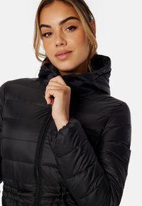 Giubbotto imbottito nero con cappuccio, caratterizzato da un design a cuciture orizzontali, zip frontale completa e una vestibilità aderente in vita. Texture liscia e lucida.