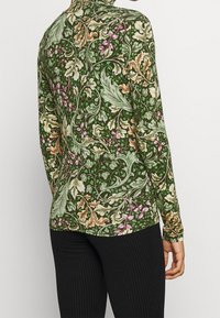 Tröja med lång ärm i mörkgrönt tyg med blommönster i rosa, kräm och gula nyanser. Har hög krage och figursydd design.