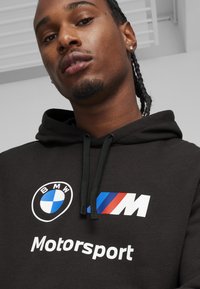 Black hoodie made of soft fabric, featuring a circular BMW logo, a colorful M logo, and "Motorsport" text in white.