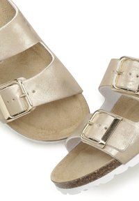 Gold metallic two-strap sandals with square buckles, soft beige insoles, and a white textured sole, featuring a cork footbed for comfort.