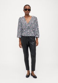 Blusa preta com flores e mangas bufantes, apresentando flores rosas e brancas, combinada com calças de couro pretas ajustadas e sapatilhas pretas.