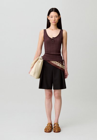 Top marrone a coste con scollo arricciato, pantaloncini larghi neri, foulard a fantasia come accessorio, borsa color crema e sandali marroni con cinturini.