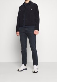 Mörkblå kordjacka med två bröstfickor, parat med slim fit mörka jeans och vita sneakers med grå detaljer.