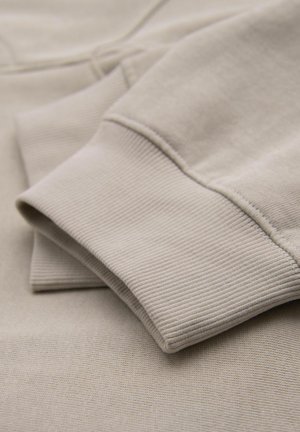 Beige bomullssweatshirtmaterial med en slät yta och ribbade ärmslut, som visar upp en vikt design och subtil textur.