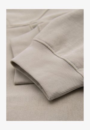 Tessuto felpa in cotone beige con una superficie liscia e polsini a costine, che presenta un design piegato e una texture sottile.