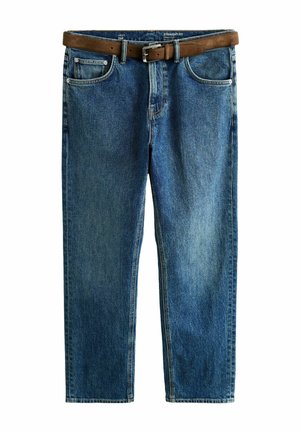 Bal kéz pihen a kék farmernadrág mellett, barna szarvasbőr övvel és fehér betűrt inggel.