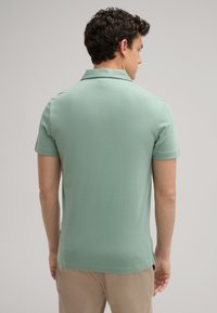 Mintgroene polo met korte mouwen, gemaakt van zachte stof, voorzien van een klassieke kraag en een rechte zoom, met een subtiele textuur.