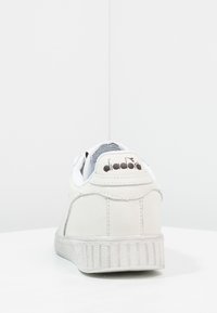 Vit lädersneaker med en texturerad yta, med en böjd häldesign och räfflad gummisula. "diadora"-logotyp på heel tab.