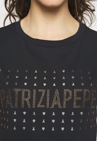 Camiseta negra con adornos metálicos en oro y plata, que exhibe el texto "PATRIZIA PEPE" y patrones decorativos de corazones y lazos.