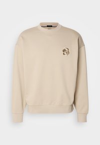 Sweat-shirt beige à manches longues avec col rond, poignets et ourlet côtelés, avec un petit logo brodé "SB" sur la poitrine gauche.