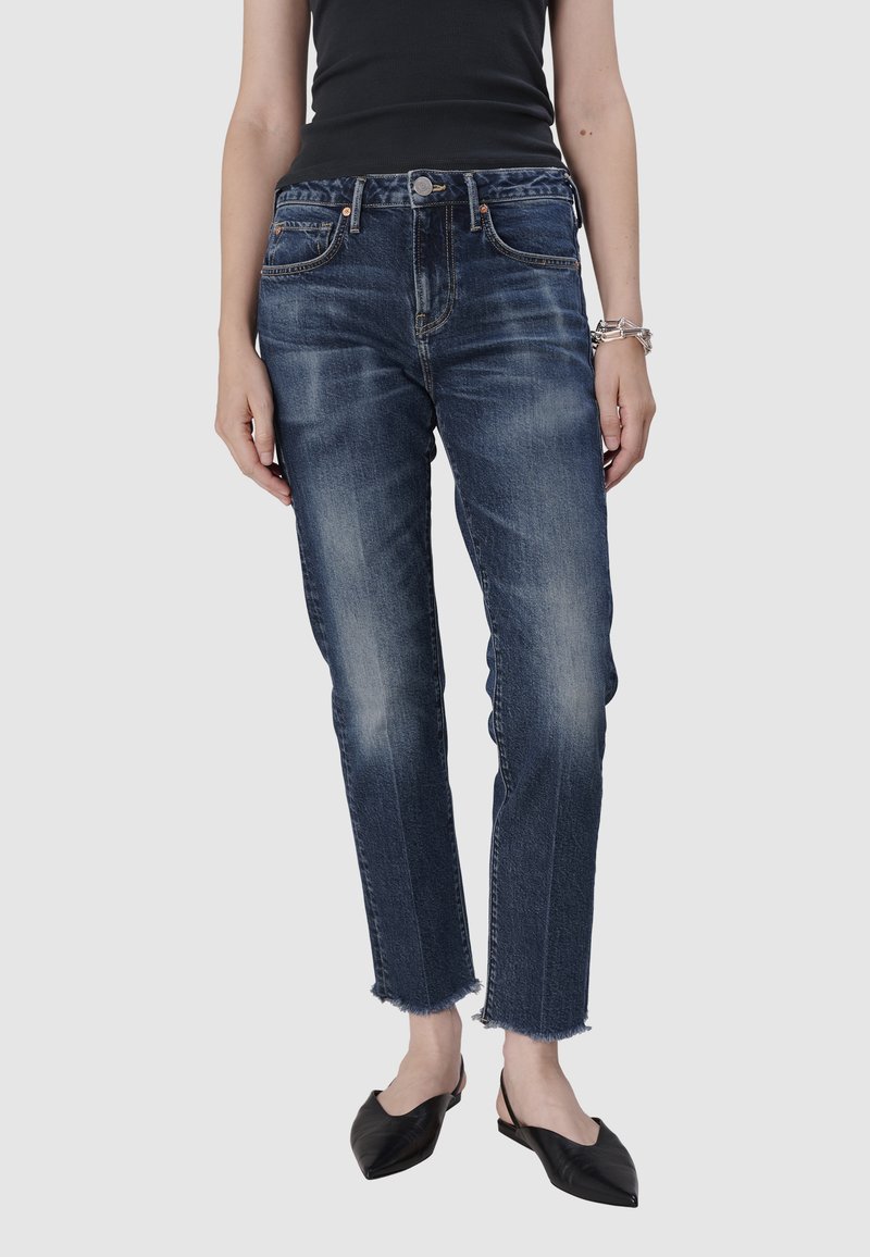 Jean en denim bleu foncé avec une légère décoloration, coupe droite et ourlet effiloché. Il présente un design à cinq poches et une fermeture à bouton métallique.