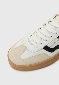 Weiße und beige Sneaker mit schwarzen Akzenten, aus Wildleder und glattem Leder, flachen Schnürsenkeln und einer Sohle aus Gummi. Mit Logo-Branding.