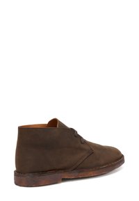 Stivaletto desert in pelle marrone con due occhielli, suola in crepe e cuciture semplici, mostrato dal lato esterno su sfondo bianco.