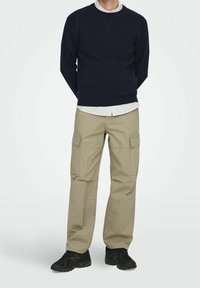 Laivastonsininen collegepaita pyöreällä pääntiellä, beiget cargo-housut sivutaskuilla ja mustat lenkkarit. Yksinkertainen muotoilu ja rento istuvuus.