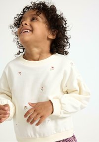 Sweter w kolorze kremowym z wyhaftowanymi kwiatami, z ryflowanymi mankietami i luźnym krojem. Miękka tekstura materiału z okrągłym dekoltem.