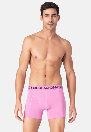 Ružové boxerky s čiernym elastickým pásom s nápisom "MUCHACHOMALO". Tkanina vyzerá hladko a má priliehavý strih.