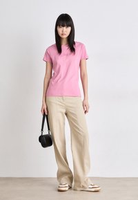 Pink cotton t-shirt with a fitted design and short sleeves, paired with light beige wide-leg trousers and multicolored sneakers. A small black handbag is held.