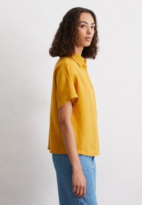 Korte mouwen, knoopsluiting shirt in een levendige mosterdkleur, gemaakt van een zachte, gebloemde stof. Kenmerkt zich door een klassieke kraag en een relaxte pasvorm.