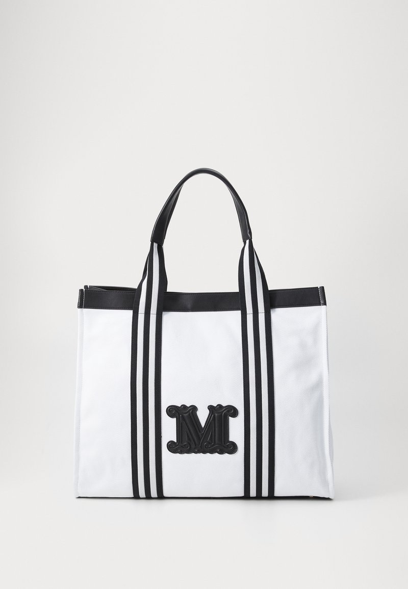 Τσάντα παραλίας από λευκό ύφασμα με μαύρες λεπτομέρειες, που διαθέτει δύο μαύρες ρίγες, ένα μαύρο διακοσμητικό γράμμα "M" μπροστά και ανθεκτικούς ιμάντες.