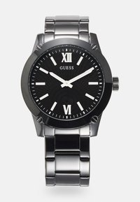 Schwarze Uhr mit rundem Ziffernblatt, silbernes Armband aus Edelstahl, römische Ziffern und ein gemusterter Zifferblatt. Markenname "GUESS" angezeigt.