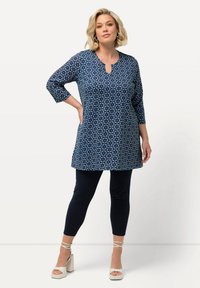 Tunique navy à motif floral, avec un décolleté en forme de clé et des manches trois-quarts, associée à un legging noir et des sandales à talons.